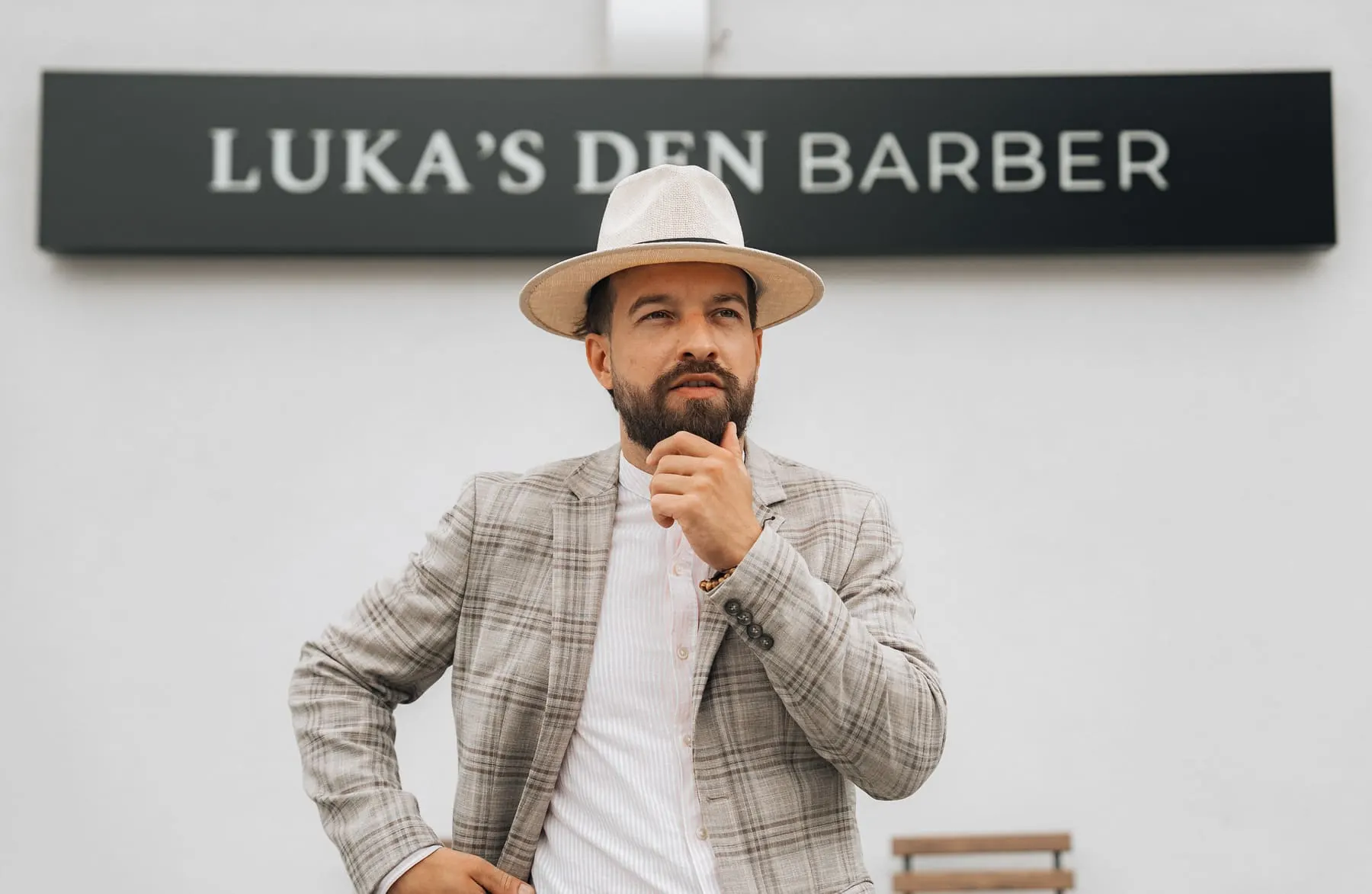 Founder & team content — Barber in a hat and checked blazer in front of the Luka's Den Barber sign — Luka’s Den — barbershop brand, Slovenia — Agency Verse