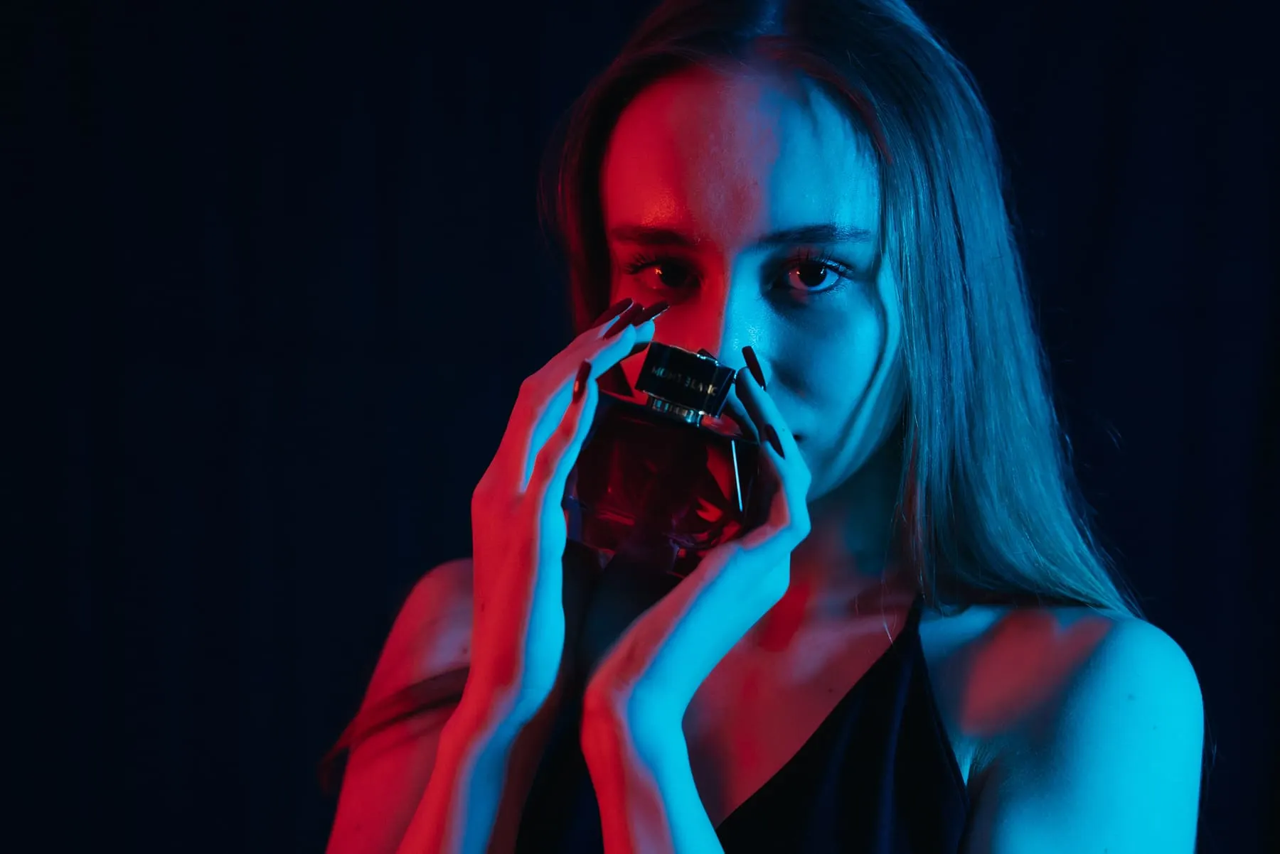 Model holding a perfume bottle in red and blue light — V Parfumes, Dubai — Agency Verse